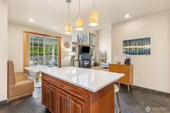 From here, the kitchen shows off its personality. The island pulls people in with casual seating, the slate floors add texture and durability, and the stainless appliances keep things current. The booth nook by the sliding door feels like a built in favorite spot, tucked right where the light comes in and close to the backyard for easy in and out. The corner sink with those two windows is one of those features you don’t realize you love until you have it, bright, open, and a little more interesting than the usual setup. Solid Cherrywood cabinets warm up the space, and everything flows naturally back into the living area.