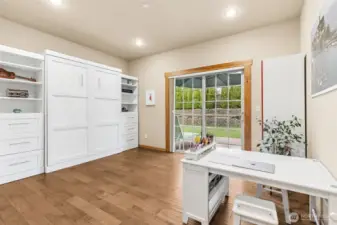 This main floor junior primary suite bedroom is pulling double duty, set up as a craft and office space right now, but with a full en suite bath it easily lives as a true guest suite or long term bedroom option. The sliding glass door brings in great light and gives direct access to the backyard and 18’ swim spa, framed by those wood wrapped details that carry throughout the home. Underfoot, the hand scraped maple floors add warmth and a little personality, paired with neutral tones that keep it easy to work with. For multigenerational living, guests who stay awhile, or just planning ahead, this is one of those spaces that quietly makes the whole house more functional.