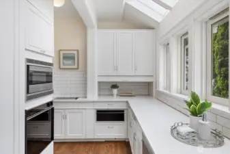 The scullery area is tucked around the corner from the kitchen. Warming drawer, induction burners for caterer or home chef, additional ovens, and walls of cupboards and shelves.