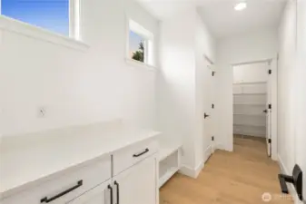 This mud room includes a built-in bench, cabinet storage, and spacious countertop area, offering a practical landing zone off the garage. High windows bring in natural light, keeping the space bright while maintaining privacy. The adjacent walk-in pantry adds extra convenience for unloading groceries and staying organized.    These photos are from Lot 3 at Gooden Hollow, which is the same floorplan. However, Lot 6 will have changes, so all photos, renderings, site maps, and floorplans are for visualization purposes only. Plans, colors, building orientation, finishes, home outlook, and other details can and WILL vary.