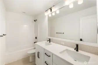 This upper-level bathroom blends clean modern lines with practical everyday function, offering dual sinks, black fixtures, and ample counter space. Its bright layout and timeless finishes make it an easy fit for busy household routines.    These photos are from Lot 3 at Gooden Hollow, which is the same floorplan. However, Lot 6 will have changes, so all photos, renderings, site maps, and floorplans are for visualization purposes only. Plans, colors, building orientation, finishes, home outlook, and other details can and WILL vary.