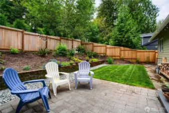 The fully fenced backyard offers a private outdoor retreat with lush landscaping, stone accents, and a spacious patio—perfect for outdoor dining, entertaining, or simply enjoying the tranquil forested setting.