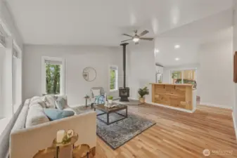 Step into a bright and inviting living space featuring vaulted ceilings, beautiful LVP flooring, and large windows that frame the surrounding greenery. A cozy wood stove adds warmth and character, creating the perfect gathering space.