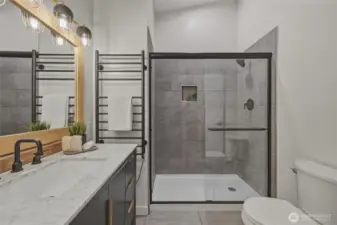 The updated bathroom features a sleek tile walk-in shower with glass enclosure, modern fixtures, a marble vanity, and a heated towel rack for a spa-like touch.