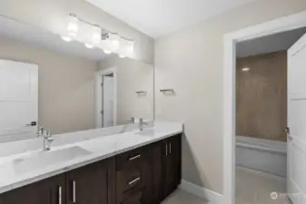 This shared main bathroom features upgraded quartz countertops, elegant tile floors, and a stunning tub with tile surround extending to the ceiling.