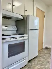 View from the entry of the kitchen showing the range, refrigerator & cabinetry.  The door shown is the door to the downstairs/basement & garage