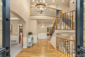 Broad double doors open to the expansive foyer, showcasing gleaming hardwood floors and vaulted ceilings.