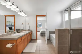 Primary bathroom with 2 sinks, tub and shower. Standing view from the primary closet.
