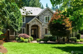 Impressive approach with steep pitched gable roof, covered entry with brick accents, and mature landscaping