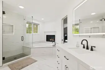 Newly remodeled, the ensuite features a designer-tiled shower with seamless glass enclosure and soaking tub in front of the fireplace.