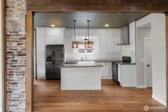 View from the living room into the kitchen, with front entry on the left and hall way to the right to main floor bedroom, bathroom, rear mud room and stairs to the lower level. The original floors, brick and beams in this home give it so much enchanting.