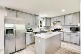 This stylish kitchen has cabinets galore, a center island for prep space, trendy backsplash and stainless-steel appliances! Notice the window above the sink that peeks to the backyard and garden beds.