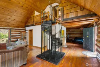 A striking wrought-iron spiral staircase anchors the great room, leading to the loft above. Surrounded by soaring pine ceilings and rustic log walls, this space blends craftsmanship with character, creating a focal point that feels both dramatic and timeless.