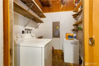 Compact laundry room with washer and dryer hookups, open shelving for storage, and exposed wood beams that tie into the rustic character of the cabin.