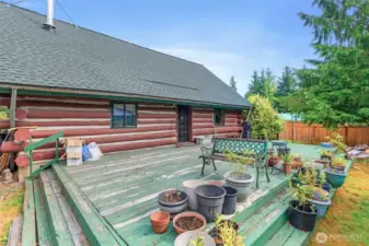 Spacious back deck offering plenty of room for outdoor living, container gardening, and entertaining. Surrounded by evergreens, this private outdoor space extends the rustic lifestyle of the log cabin.