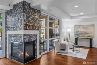 Bright and airy living room with floor-to-ceiling windows, cozy fireplace, and peek views of the Seattle skyline and mountains.