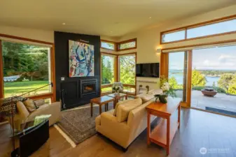 Living area with wood-burning fireplace, pass-through wood closet, frame tv, and sliding doors that lead out to the west-facing patio overlooking Fisherman Bay and San Juan Channel.