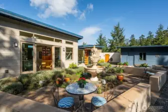 The enclosed garden, the main home on the left and the oversized garage, to the right, with the private entryway to the enclosed space seen just to the right of the fountain. The raised beds off to the middle right are irrigated by a catchment system.