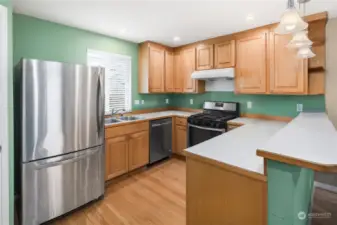 Well-equipped kitchen with stainless steel appliances, gas range, wood cabinetry, and a functional breakfast bar.