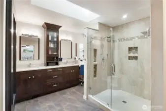 The primary bathroom was designed with comfort and style in mind—from the custom tile walk-in shower with built-in seat and dual niches to the dual vanities and abundant cabinet space. A well-placed skylight keeps the space naturally bright while enhancing the serene feel of this private retreat.
