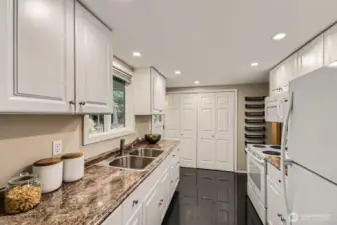A beautiful kitchen with tile floors, white cabinetry, stainless steel sink and beautiful countertops, with a window looking into the tranquil back yard. The door leads to to the entertaining back deck.
