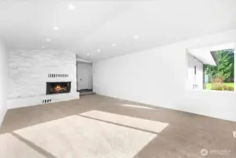 An alternate view of your bright and airy living room with vaulted ceilings, recessed lighting, a cozy wood burning fireplace. Tons of natural light with abundance of windows and space. Hallway past fireplace leads to bedrooms on the right and dining room and kitchen to the left.