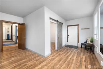 View from open living space toward front door on right with sliding barn door leading to additional room. Door to far left leads to a flex room and a 3/4 bathroom.