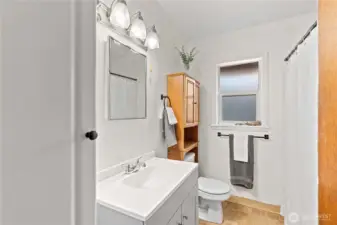 Stylish and functional bathroom featuring a modern gray vanity, ample storage, and tasteful fixtures. A large mirror with overhead lighting, tiled flooring, and natural accents create a clean and welcoming space. Bathtub/shower combo, convenient stacked washer and dryer unit finish out this bathroom