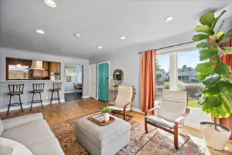 Living space with abundant natural light coming through picture windows. Looking out toward front door and kitchen space