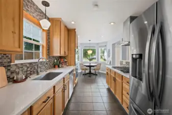 Galley kitchen with fridge, sink overlooking the backyard, gas stovetop, double-oven, eating nook at end of kitchen.