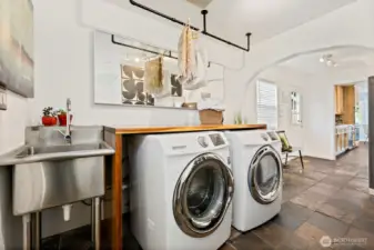 Utility room with front load washer & dryer, wood countertop for folding, and stainless utiity sink, and ceiling mounted drying racks. View looking out to mudroom and side patio access door off kitchen.