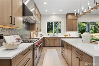 Warm wood cabinetry to ceiling, serene backdrop from the kitchen window and patio slider. 48" Wolf range, slab quartz countertops, under-cabinet lighting, island chandelier, in-island sink, and commercial grade stainless-steel hood.
