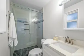 The primary bathroom includes a modern three-quarter layout with an updated vanity, stylish fixtures, and a walk-in shower with sliding glass doors.