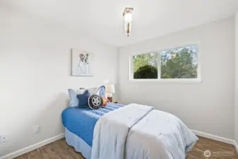 One of two additional bedrooms provides a flexible layout for a guest room, home office, or personal space. Its large window overlooks greenery, enhancing the sense of privacy.