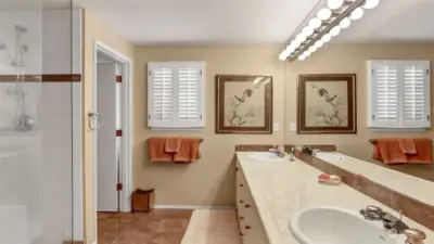 Large primary bathroom with gleaming floors and tile countertops. His and her sinks. Huge walk in custom dual head shower. Toilet has it's own door for privacy.