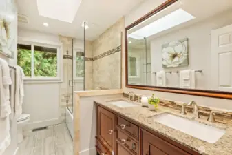 Remodeled guest bath with dual vanities, skylight, and warm tile accents.