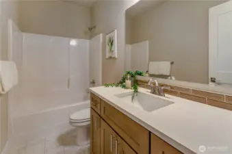 This beautifully appointed full bathroom includes a vanity with a below quartz surface mounted sink and easy-to-clean bath/shower