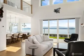 The heart of the home, this stunning great room showcases soaring ceilings and an entire wall of view windows. Flooded with natural light, the space seamlessly blends indoors with the surrounding beauty—Puget Sound, Olympic Mountains, and unforgettable sunsets become part of your everyday living.the sparkling waters of Puget Sound & Admiralty Inlet