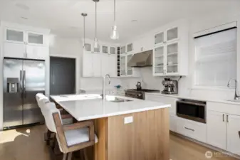 This beautifully designed wood island serves as the heart of the kitchen. Equipped with a sink, dishwasher, and seating, it blends functionality with style, providing a perfect workspace and casual dining area. Its warm wood tones contrast elegantly with the surrounding white cabinetry, creating a visually striking and practical centerpiece for cooking, entertaining, and enjoying waterfront views.