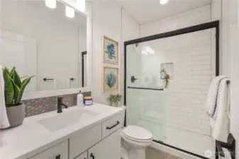 Lower Level Bathroom  This lower level main bathroom features a clean, modern design with quartz countertops, a sleek undermount sink, and matte black fixtures for contrast. A tiled shower with glass enclosure and built-in niche adds both function and architectural simplicity, while durable flooring supports everyday use.    Located in Bothell’s Canyon Park area, this full bath enhances the versatility of the lower level, allowing the adjacent den to function comfortably as a guest suite or additional bedroom. The thoughtful layout reflects the practicality and finish quality expected in modern new construction within the Northshore School District.    These photos are from a past Robinson Plan at a different community, so overall plan, colors, building orientation, finishes, home outlook, and other details can and WILL vary. All photos, renderings, site maps, and floorplans are for visualization purposes only.