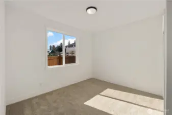 Main Level Den / Guest Bedroom  This main level den offers flexible living space with clean lines and abundant natural light. A large window frames the backyard outlook while soft carpeting and neutral tones create a comfortable setting for a home office, guest suite, or additional bedroom. The thoughtful placement on the main level enhances everyday convenience and accessibility.    Situated in Bothell, Washington near Canyon Park, this versatile room supports modern living within a Pacific Northwest contemporary home. The adaptable layout reflects the intentional design approach found in luxury new construction served by the Northshore School District.    These photos are from a past Robinson Plan at a different community, so overall plan, colors, building orientation, finishes, home outlook, and other details can and WILL vary. All photos, renderings, site maps, and floorplans are for visualization purposes only.