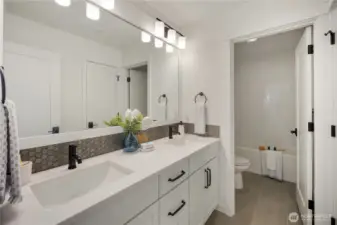 Upper Level Secondary Bathroom  This upper level secondary bathroom features a dual-sink vanity with quartz countertops, matte black fixtures, and a full-width mirror that enhances light and scale. Clean cabinetry lines and durable tile flooring create a streamlined, low-maintenance design suited for everyday use.    A separate enclosed tub and toilet area provides added privacy and functionality, supporting shared use with ease. Located in Bothell’s Canyon Park neighborhood, this well-appointed bath reflects the thoughtful planning associated with modern new construction homes served by the Northshore School District.    These photos are from a past Robinson Plan at a different community, so overall plan, colors, building orientation, finishes, home outlook, and other details can and WILL vary. All photos, renderings, site maps, and floorplans are for visualization purposes only.