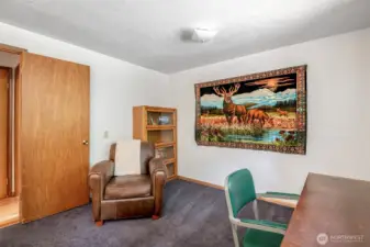 This bright and restful bedroom is bathed in natural light, with soft white walls, warm wood accents, and peaceful wooded views out the window.