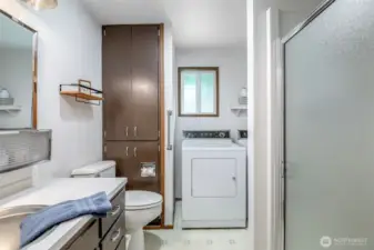 Main floor bathroom and laundry combo with full-size washer/dryer, built-in linen storage, and a walk-in shower—efficient and practical layout.