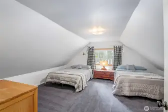 First upstairs bedroom with vaulted ceilings and dormer windows, comfortably fits two beds and offers a perfect hideaway feel for guests.