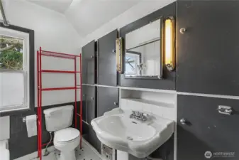 Functional bathroom with older fixtures, black cabinetry, and a bold red shelving unit, offering natural light and a practical layout ready for cosmetic updates and personalization.
