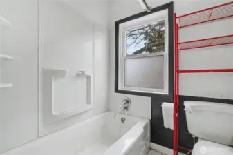 Full bathroom featuring a tub/shower combo with built-in shelving, classic tile accents, and a window for added light and ventilation—an efficient space with opportunity for modern upgrades.