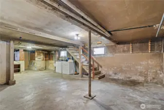 Unfinished basement with exposed beams, concrete floors, and laundry hookups—ideal for storage, workshop use, or future finishing to expand usable living space.