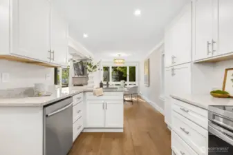 The fully remodeled kitchen opens to a dining area filled with natural light and tree views, creating a seamless space to gather.