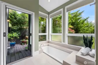 Unwind in the deep soaking tub, surrounded by windows bringing in natural light, looking onto the lush, private landscaping and tranquil outdoor atrium.